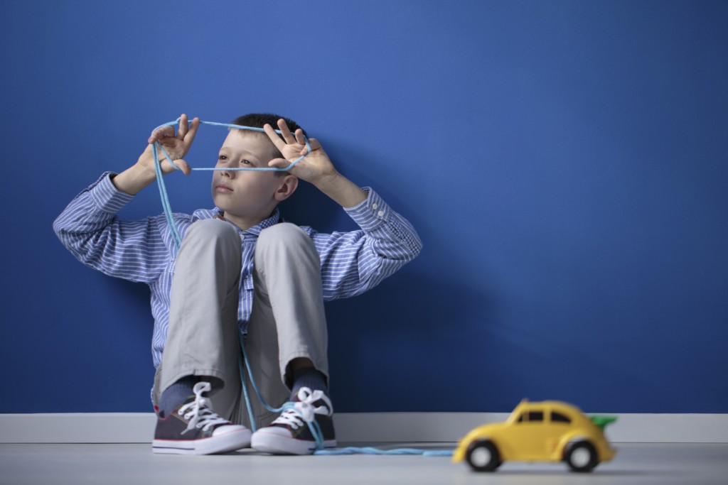 enfant autiste qui joue seul sans sa chambre bleu avec une voiture jaune